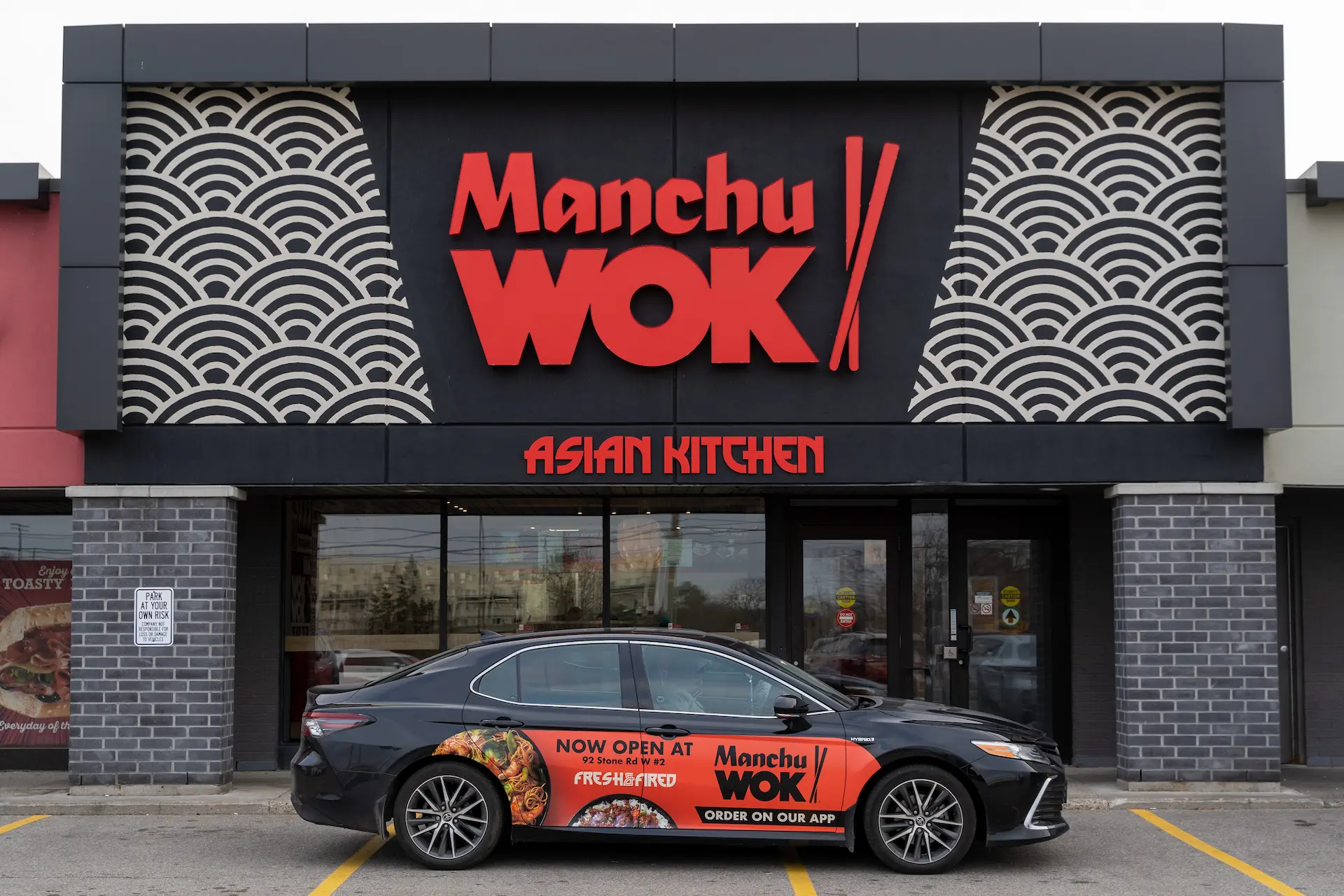 Manchu WOK Asian Kitchen street-front location with red branded signage and decorative wave pattern panels on a dark exterior facade.