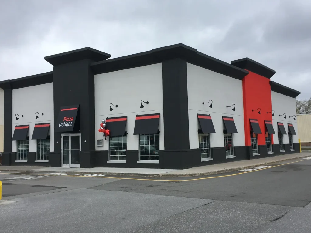 Façade extérieure d'un restaurant Pizza Delight autonome, avec enseigne rouge et noire et stationnement.